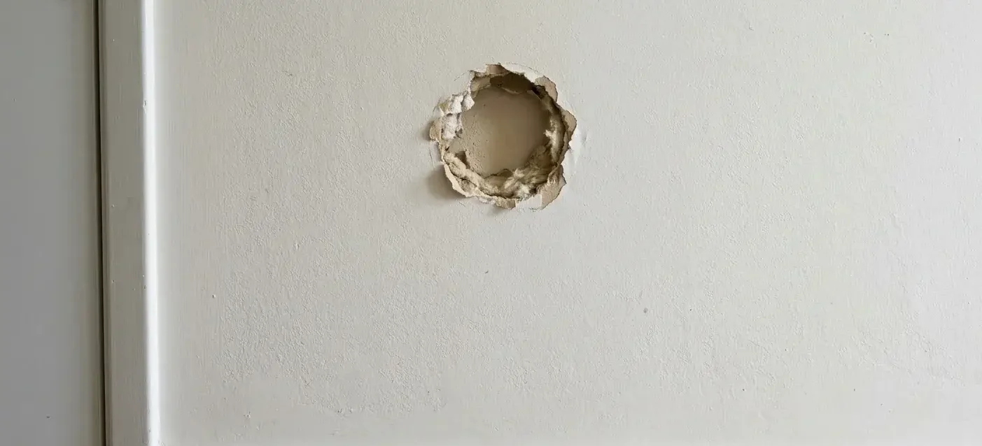Round doorknob-sized hole in painted drywall wall in a hallway
