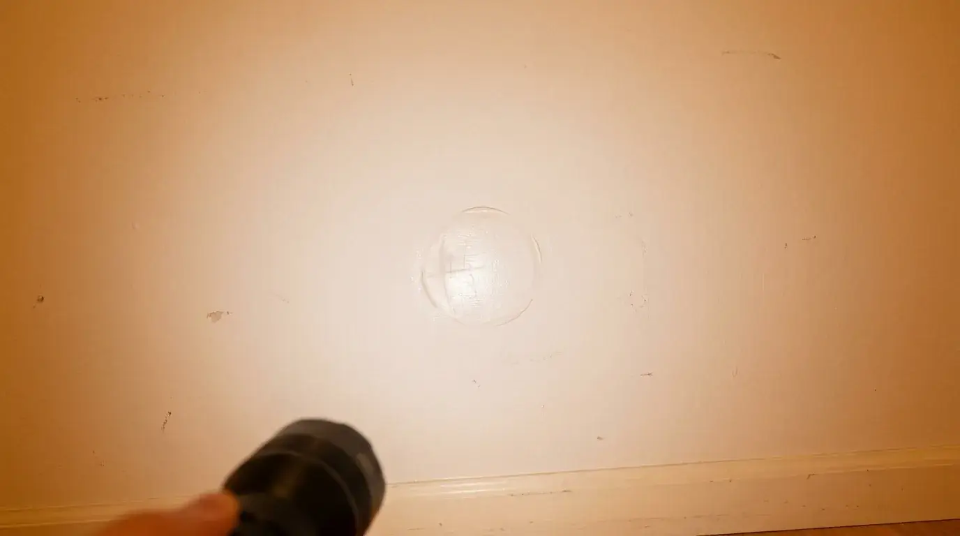 Side light reveals a raised outline on a drywall patch near doorknob height above a baseboard.