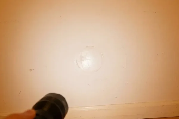 Side light reveals a raised outline on a drywall patch near doorknob height above a baseboard.