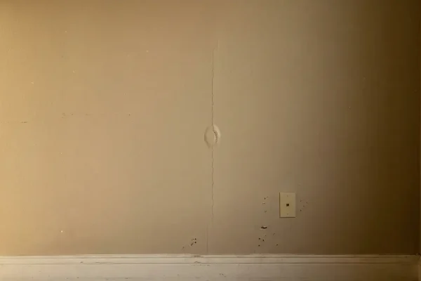 Hairline crack and small tape bubble along a drywall seam on an interior wall in raking light.