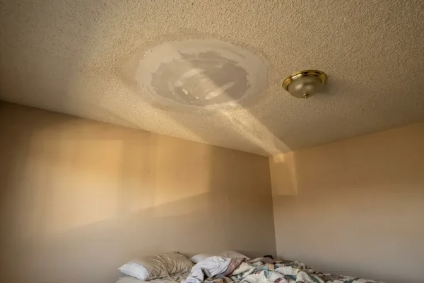 Raking light reveals a visible halo and slight ridges around a ceiling drywall patch near a room corner.